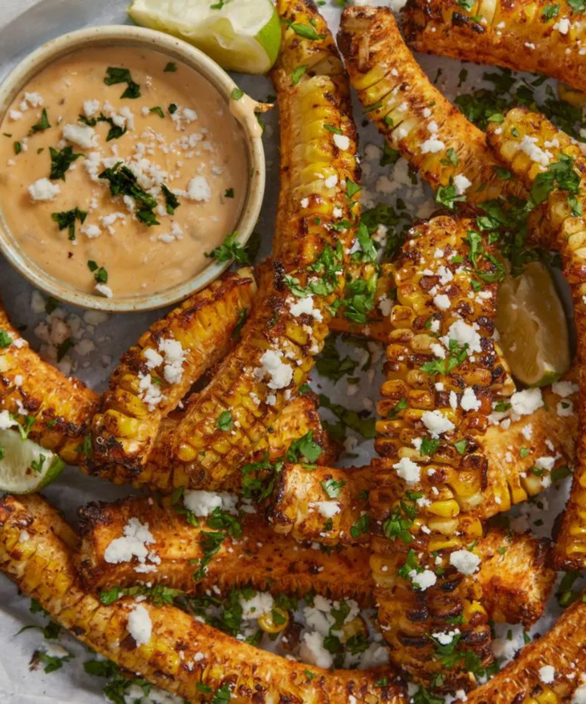 Corn ribs cooked on a grill, seasoned and serves with lime, cilantro, and sauce