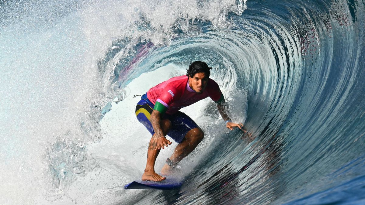 Brazil&#039;s Gabriel Medina rides in the barrel of a wave, in a red shirt and blue shorts on a blue surfboard, at the Paris 2024 Olympic Games, in Teahupo&#039;o, Tahiti.