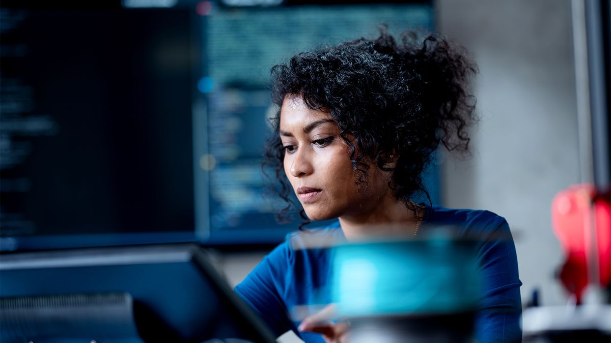 Female software developer using AI tools on a desktop computer in an open plan office space.