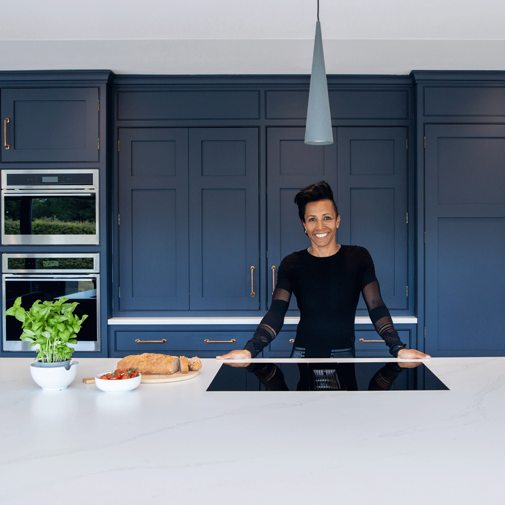 Female standing in a blue open plan kitchen with a hanging cone shaped light