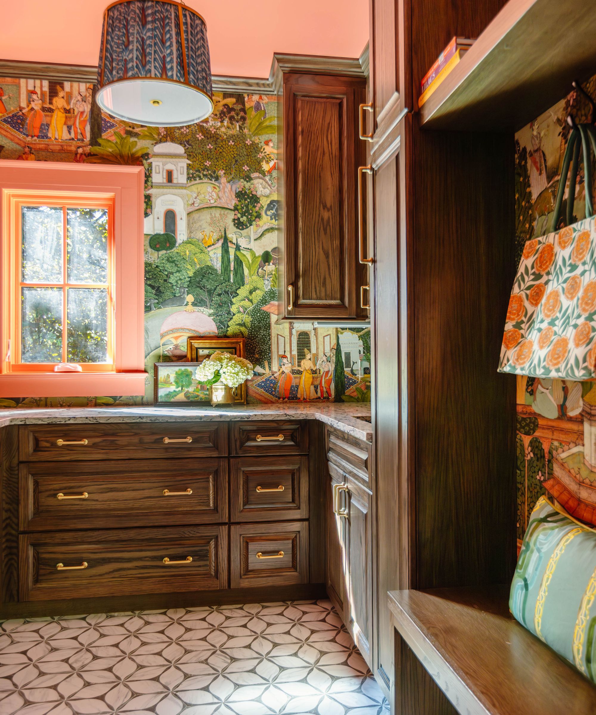 Laundry room with mahogany wood built-in drawers, cabinets, and a built-in bench, Mughal-inspired mural wallpapered walls, a coral ceiling and coral painted window trim, and a chevron tiled floor