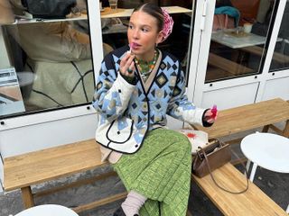 a woman wears a colorful printed jacket with a green skirt