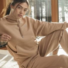A woman in a beige tracksuit sitting on the floor.