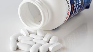 Bottle of glucosamine tablets spilled on white surface