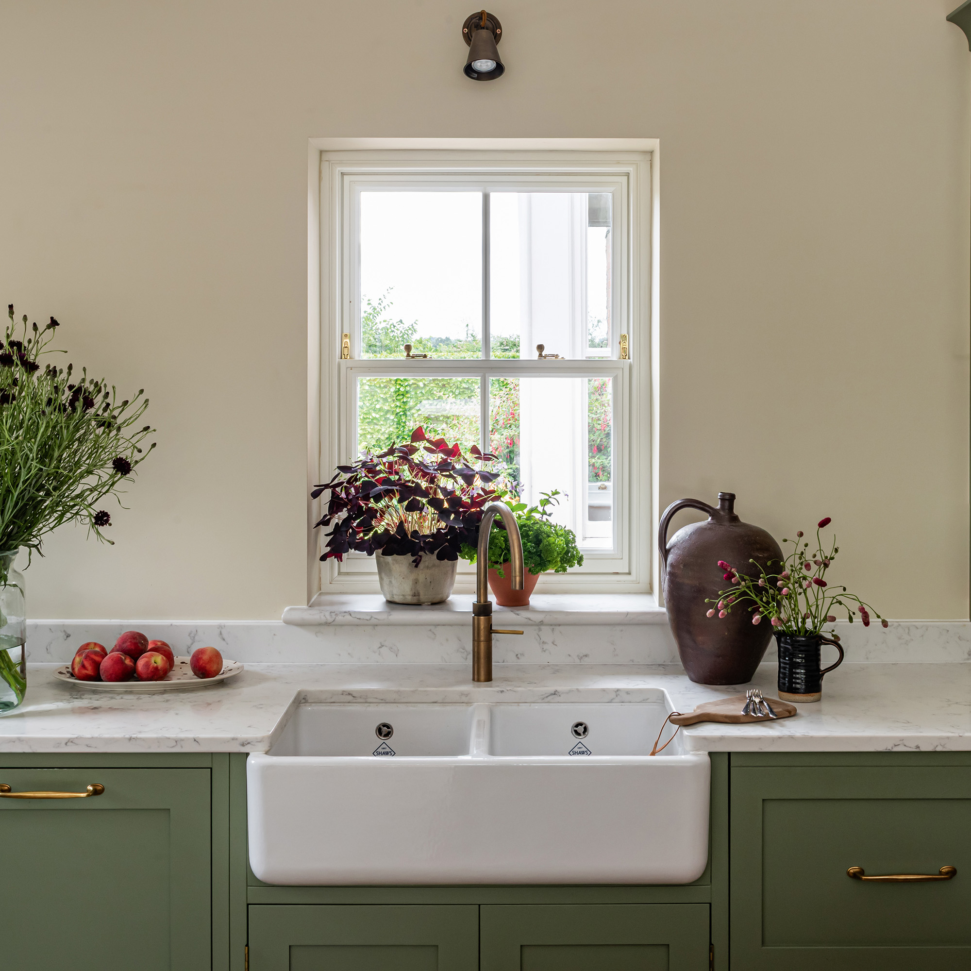 kitchen with cream wall green cabinetry and belfast sink in front of window