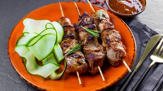 Barbecued meat on skewers on plate with salad
