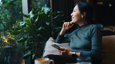A woman sits in her living room and looks out the window, looking confident.