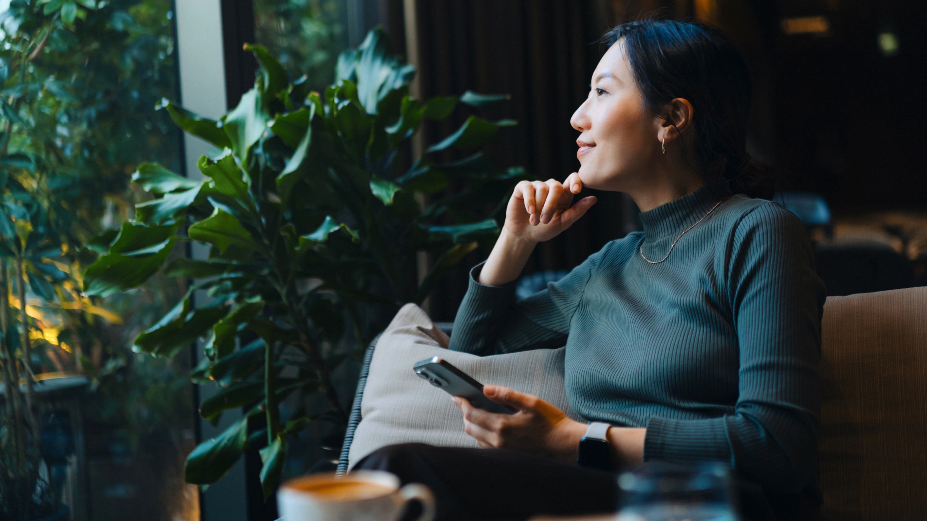 A woman sits in her living room and looks out the window, looking confident.