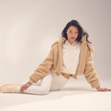 a brunette woman in a white outfit and beige jacket