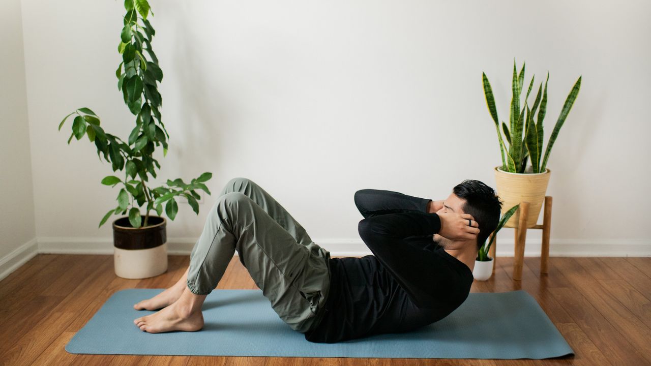 Man doing sit-ups on a yoga mat in front of two leafy plants