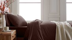 Dark brown bedding on a wooden bed with a wooden bedside table decorated with a vase of orange berries