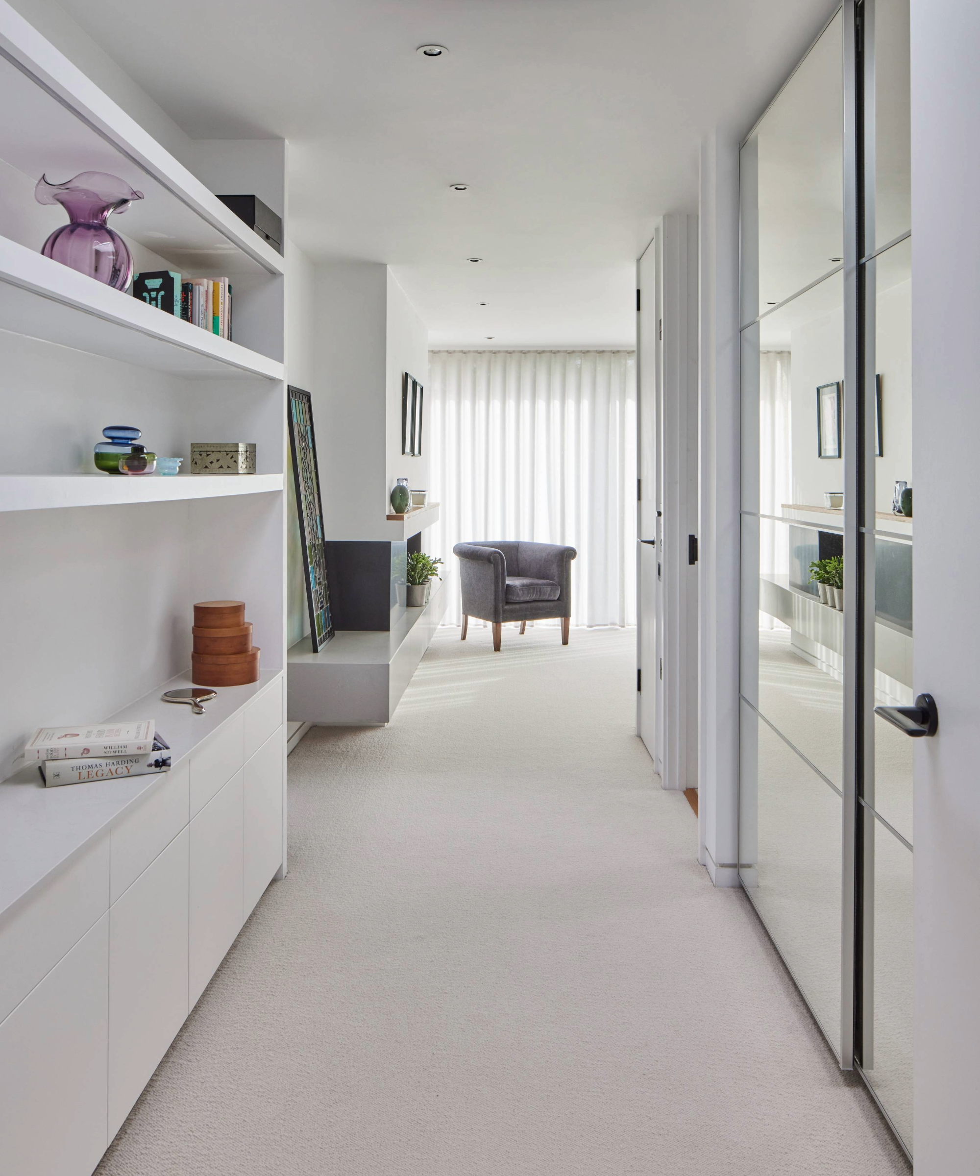 Dressing room with a mirrored wardrobe opposite shelves and cabinets