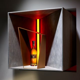 Bottle of whisky in a wooden angular frame, yellow strip back light with red outer glow, grey stone display unit