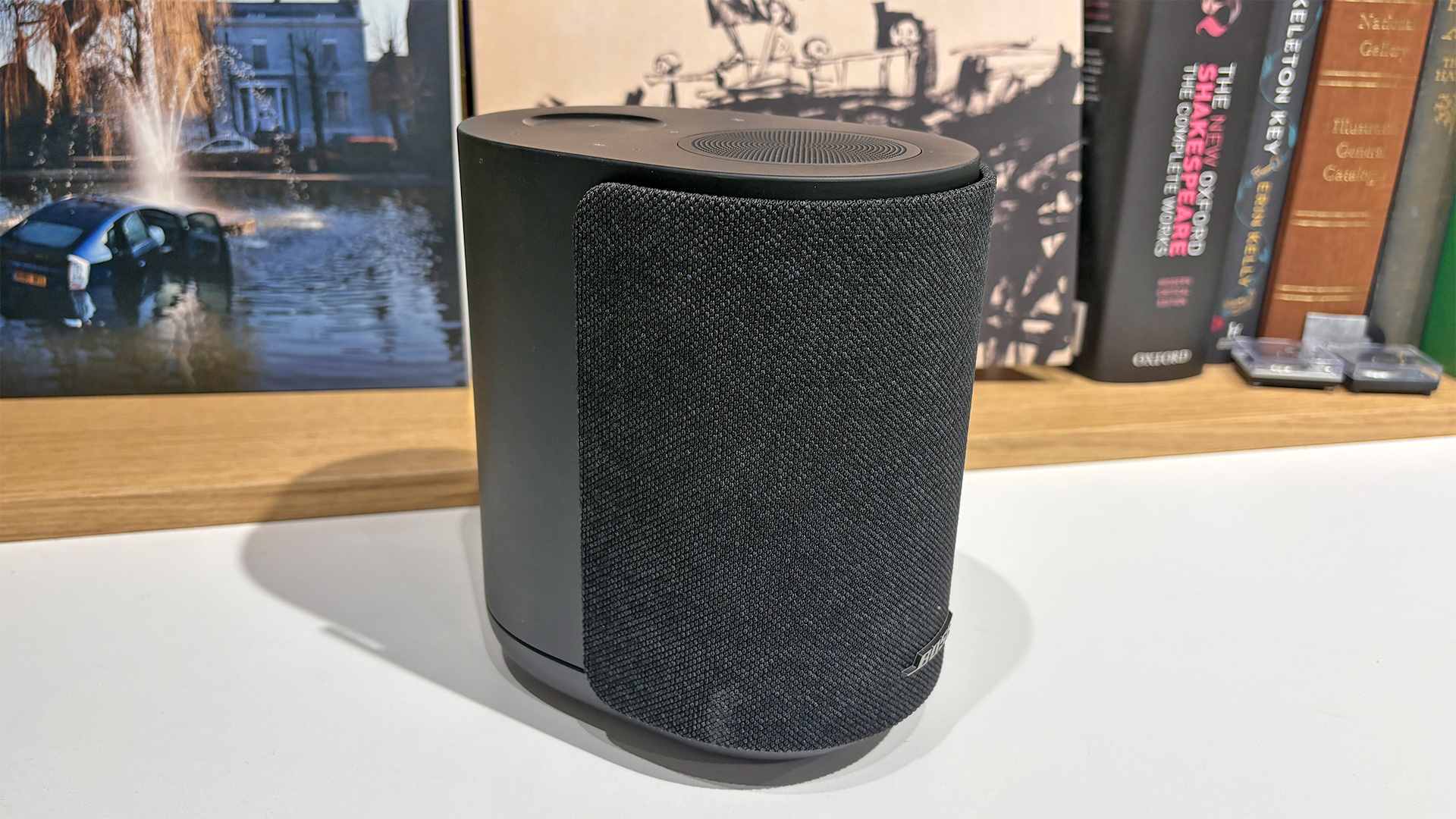 Bose Lifestyle Ultra Speaker wireless speaker on white surface in front of busy bookshelf