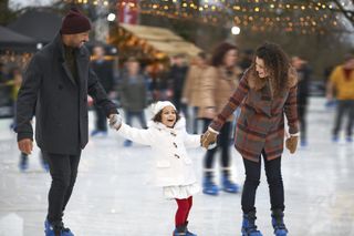 A family of three holding hands while ice skating together.