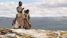 A small family of early modern humans stands on a mountain looking out over a valley