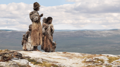 A small family of early modern humans stands on a mountain looking out over a valley