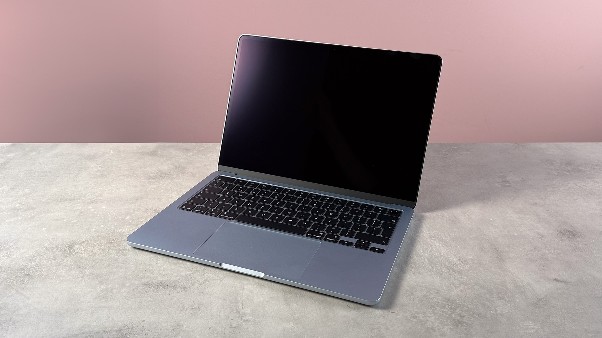 The MacBook Air M5 with a black screen in front of a pink background.
