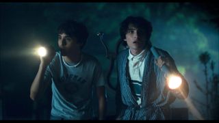 two teenage boys including finn wolfhard walking with flashlights in the dark in a still from hell of a summer