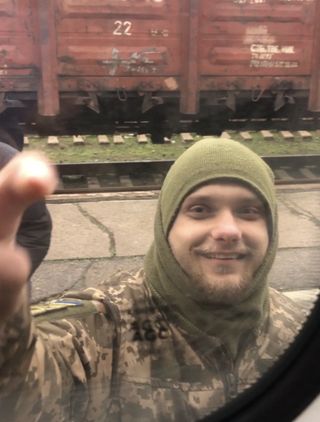 A man in army uniform taps a train window to say goodbye