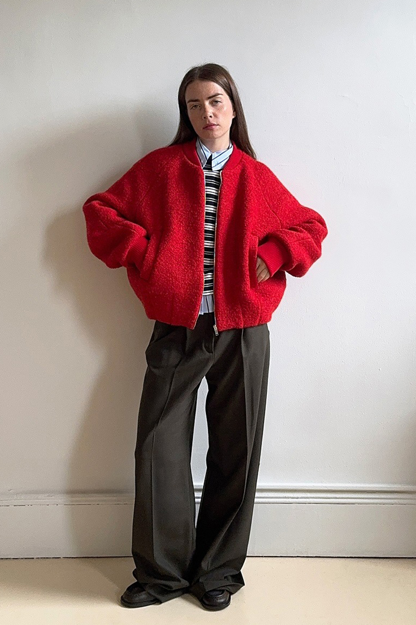 a woman wearing a red jacket, striped shirt, black pants, and black shoes