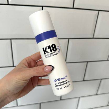 Image of a handheld view of the K18 AirWash Dry Shampoo against a white tiled background 