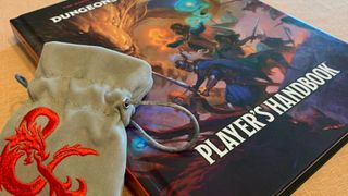 A D&amp;D Player&#039;s Handbook lying on a table, with a pouch bearing the D&amp;D logo leaning against it