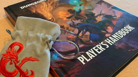 A D&D Player's Handbook lying on a table, with a pouch bearing the D&D logo leaning against it