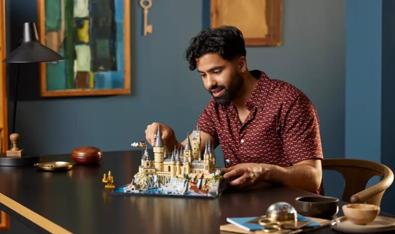 En man sitter vid ett bord och bygger ihop Hogwarts-slottet i Lego.