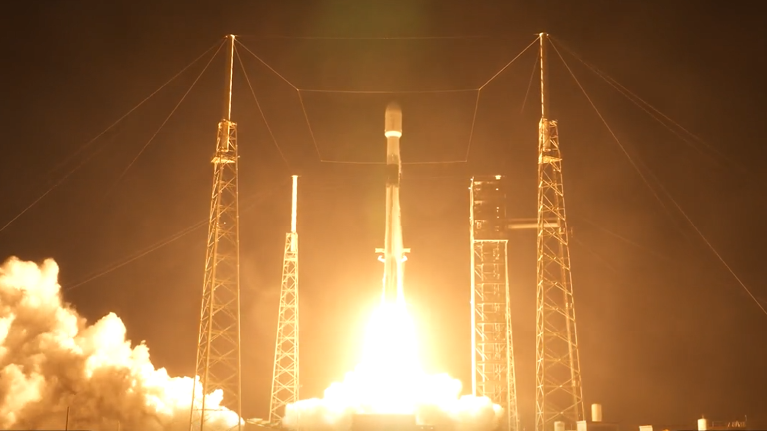A white rocket blasts off a launch site in the dark early morning. 