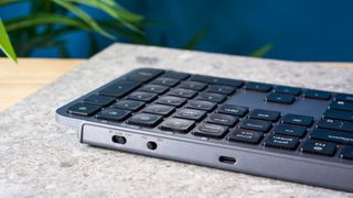 a black and grey budget wireless Bluetooth keyboard with a full-size layout and a numerical keypad is photographed against a blue background