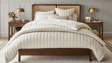 Wooden bed with cream duvet, rattan headboard, neutral color scheme and and brass lamps on wooden bedside tables