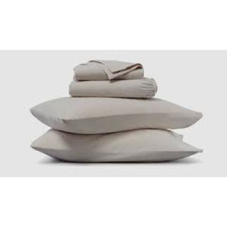 A pile of bedding. Two pillows on the bottom with two folded sheets stacked on top in a greige color