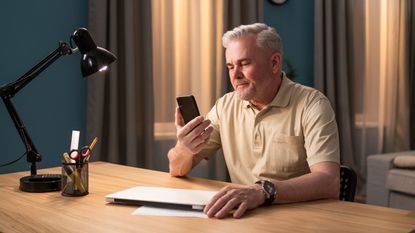A man looks at his phone while sitting at a desk. 