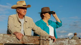 Darby and Joan watching an outdoor event with cowboy hats on.