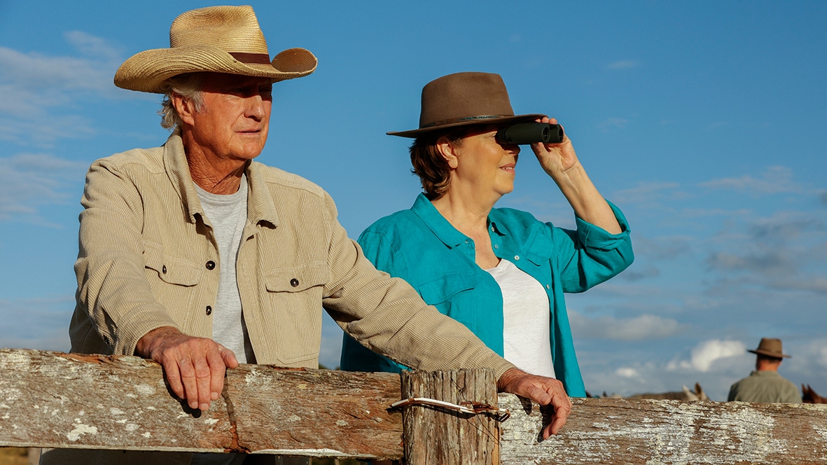 Darby and Joan watching an outdoor event with cowboy hats on. 
