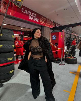 Ashley Graham wearing a coat, sheer top, leopard bra, trousers, and Puma black Speedcat OG sneakers in the pitlane at the Las Vegas Grand Prix in 2024.