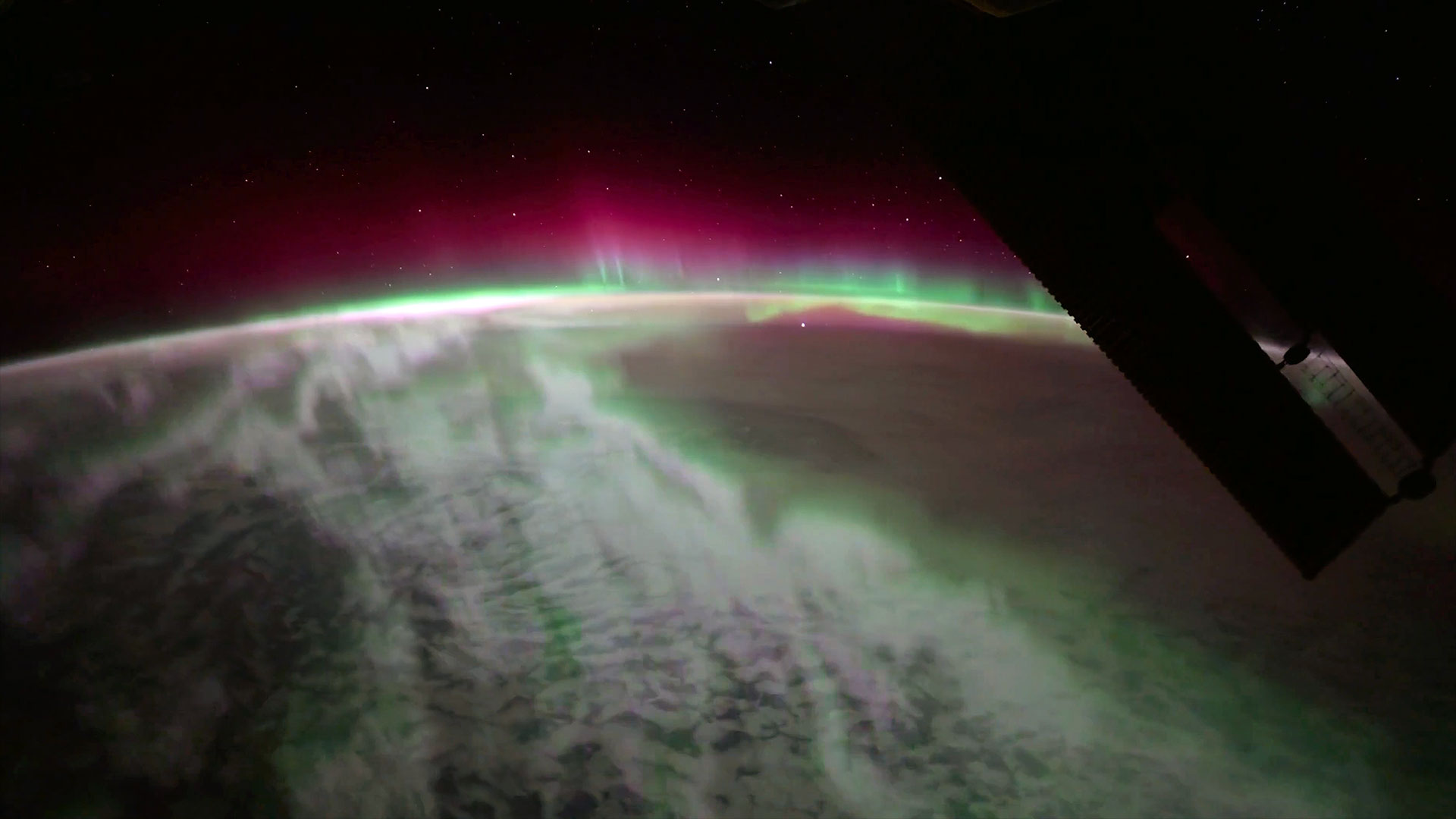 pink and green aurora shine over Earth from the vantage point of a space station