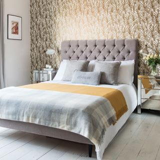 Neutral grey and white bed with yellow throw blanket in front of patterned wallpapered wall