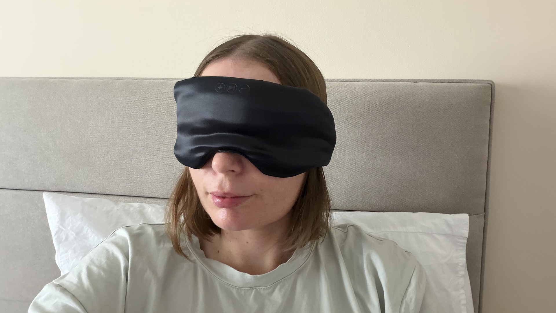 Reviewer Ruth Jones sits up in bed wearing the SilkSound Sleep Mask