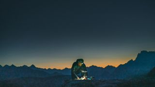 Does it really take longer to cook an egg at altitude?: man cooking on mountain ridge