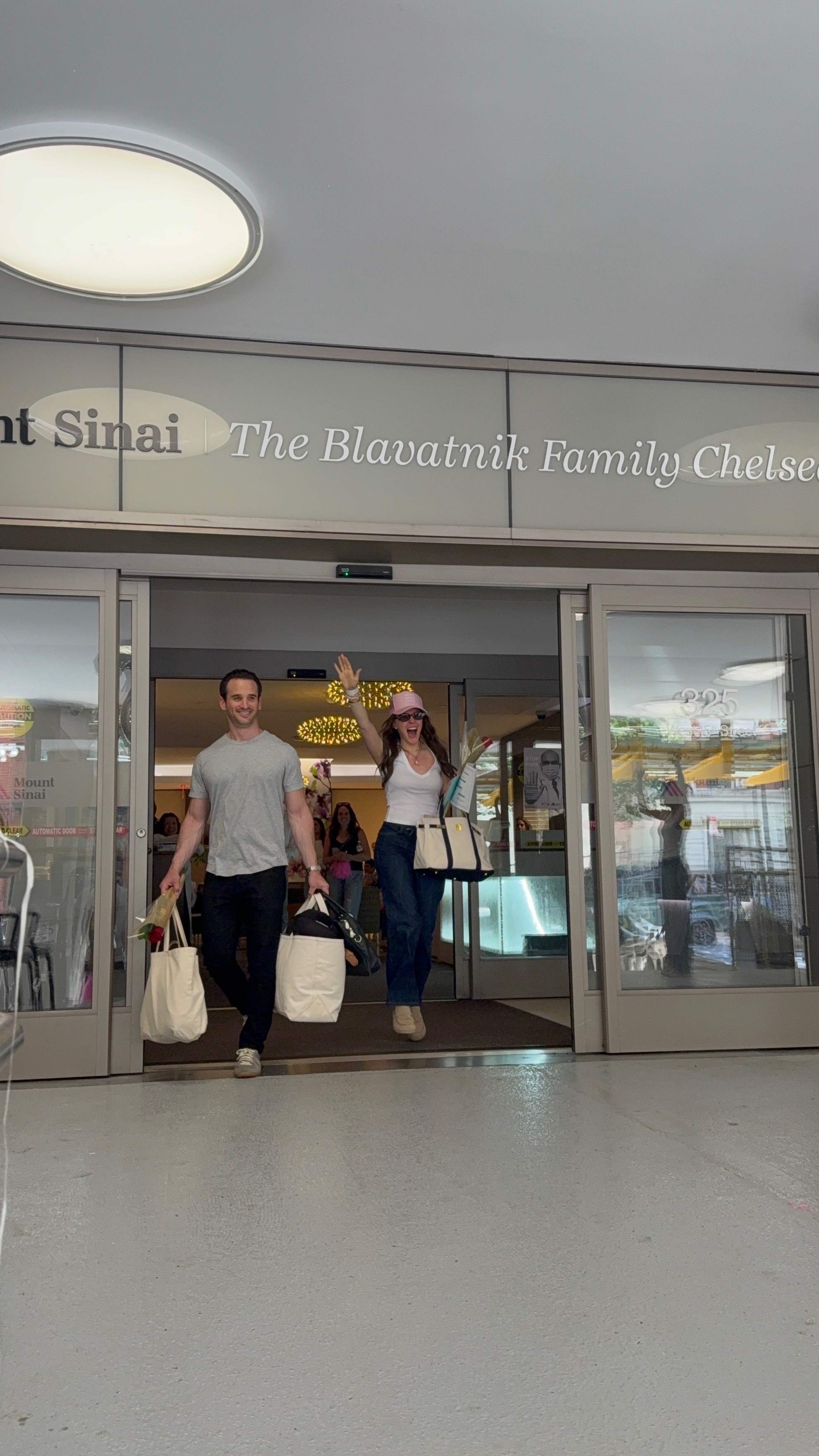 a white man and woman leaving the hospital in jeans and t-shirts carrying tote bags