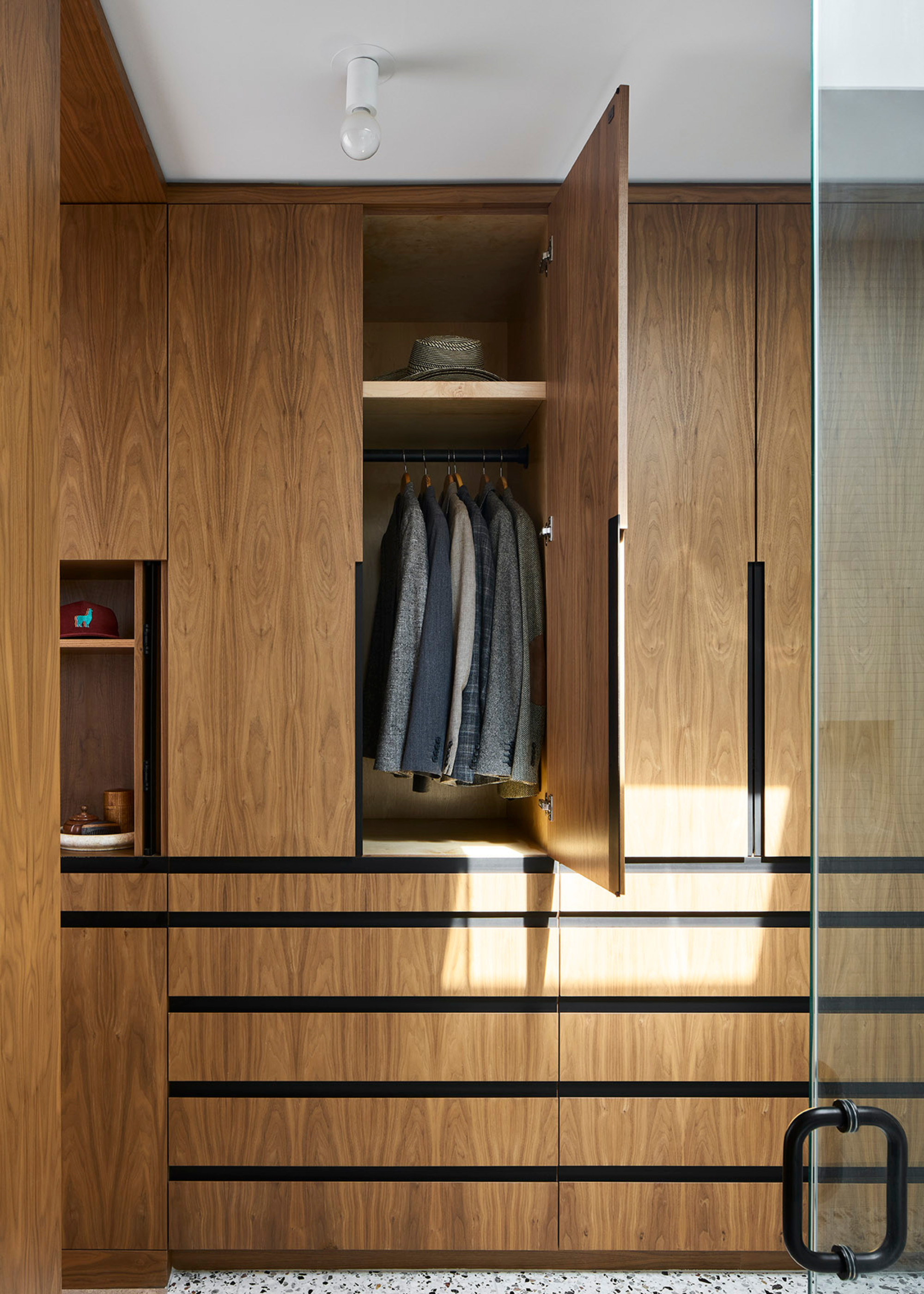 A wooden wardrobe with an open door revealing hanging suits