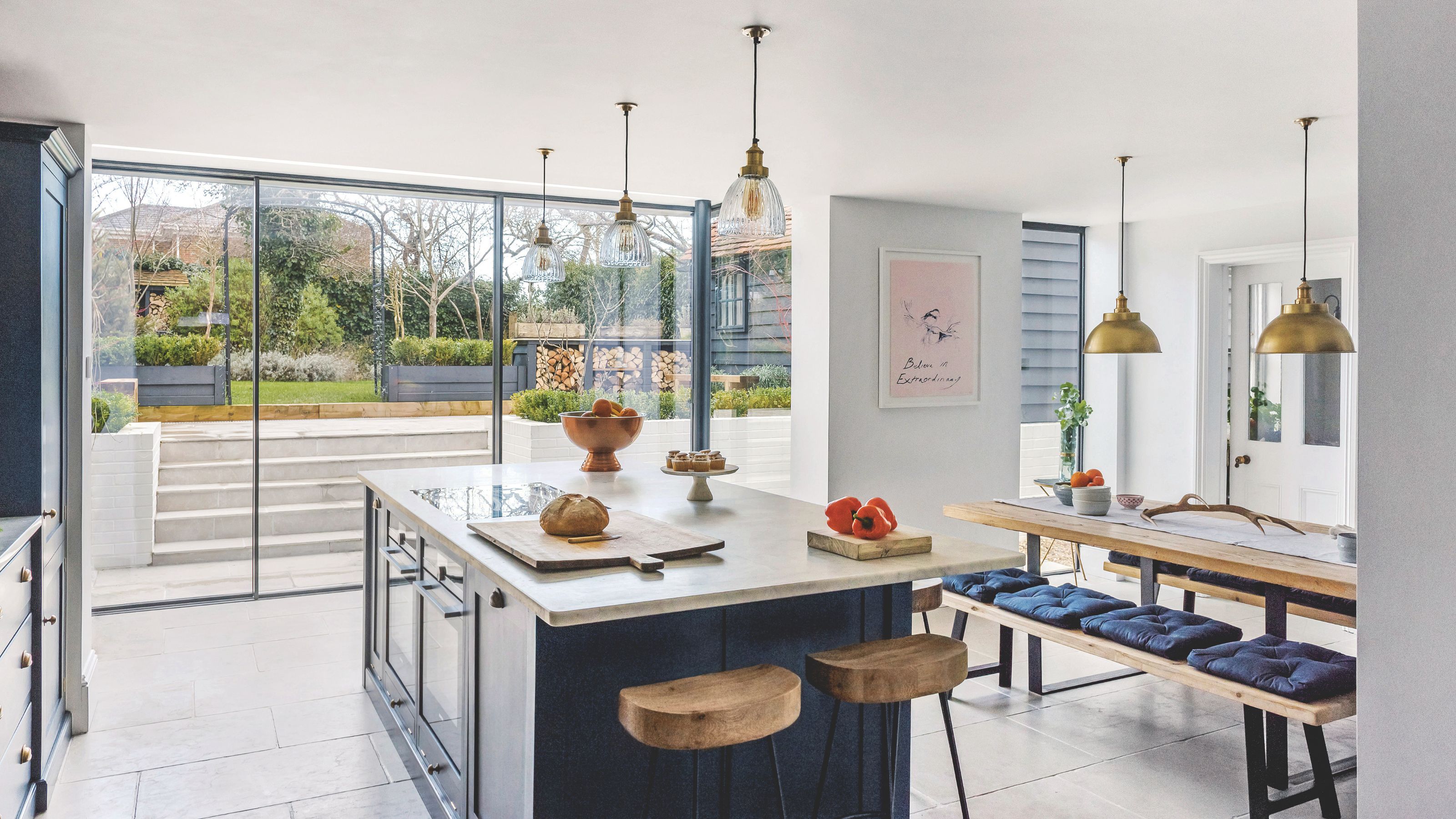 Open plan kitchen diner with navy units and island, pendant lights and large sliding patio doors