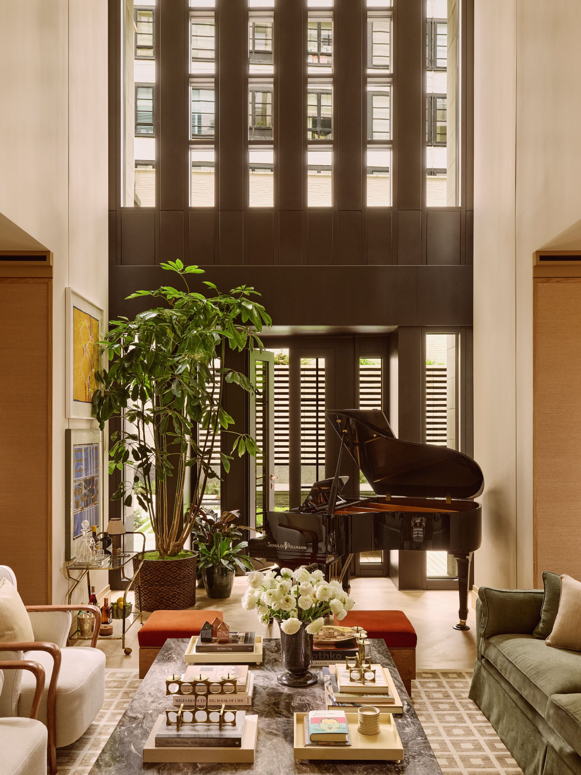 a great room with a large green plant, a piano, a marble coffee table with books, trinkets, and flowers resting on top, and accent chairs, a sofa, and ottomans around the sides