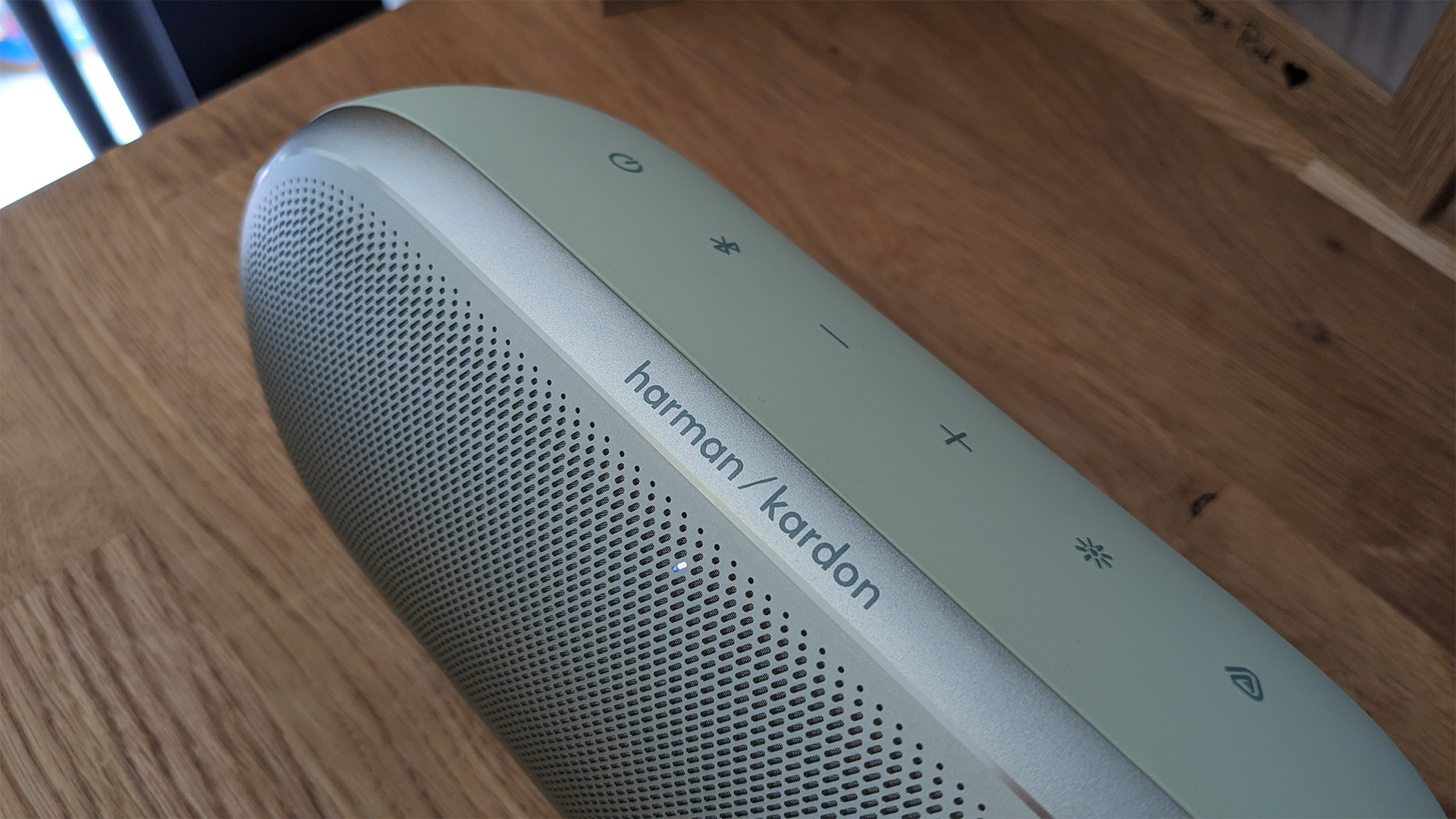 Harman Kardon Luna 2 wireless speaker on wooden table focus on Harman Kardon logo
