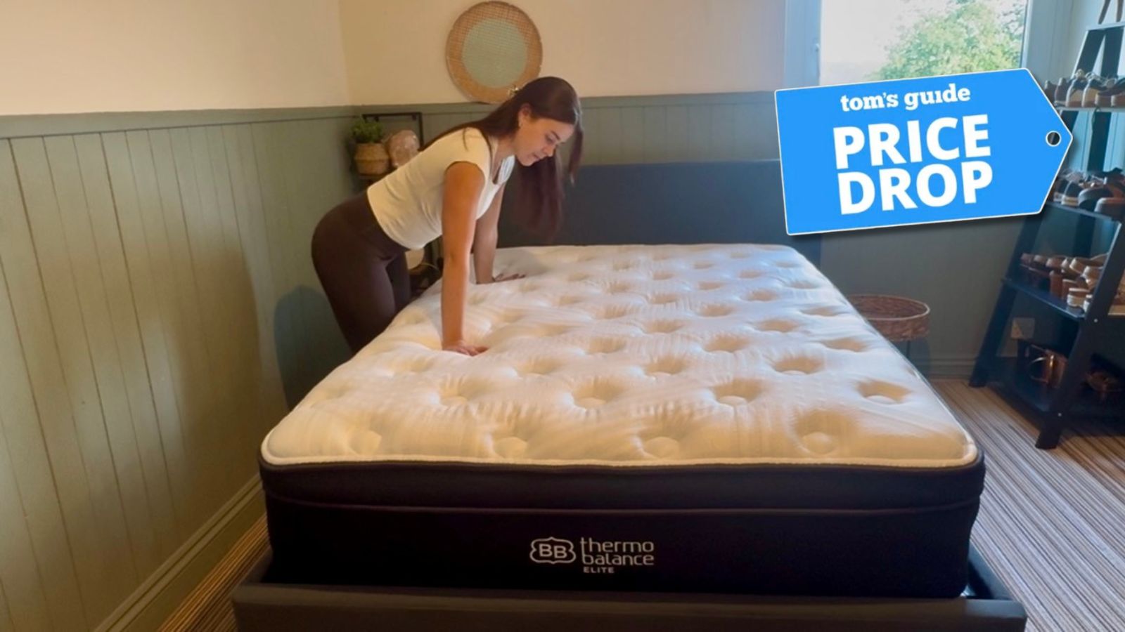 Our mattress reviewer testing the edge support on the Brooklyn Bedding Thermobalance LX Elite in bedroom with green panelled walls, with Tom's Guide 'price drop' logo