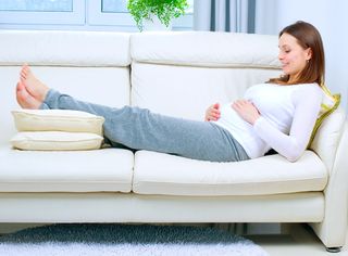 A pregnant woman rests on a couch with her feet elevated.