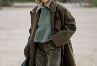 woman in olive green coat, corduroy pants, and sweater