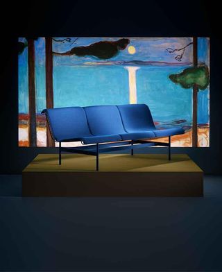 A blue sofa at the Munch Museum, shown on a low plinth in front of a landscape painting by the Norwegian artist